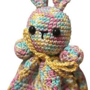 Ein gehäkeltes Häschen aus buntem Garn in Pastelltönen und mit gelbem Rand, mit großen Ohren und schwarzen Knopfaugen.