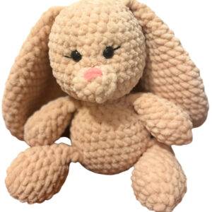 Ein plüschiges, beiges Strickhasenspielzeug mit langen Schlappohren, schwarzen Knopfaugen und einer rosa Nase, das aufrecht vor einem weißen Hintergrund sitzt.