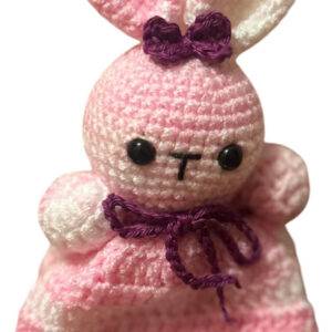 Ein rosa-weiß gehäkelter Hase mit schwarzen Augen, einer lila Schleife auf dem Kopf und einem passenden lila Band um den Hals.
